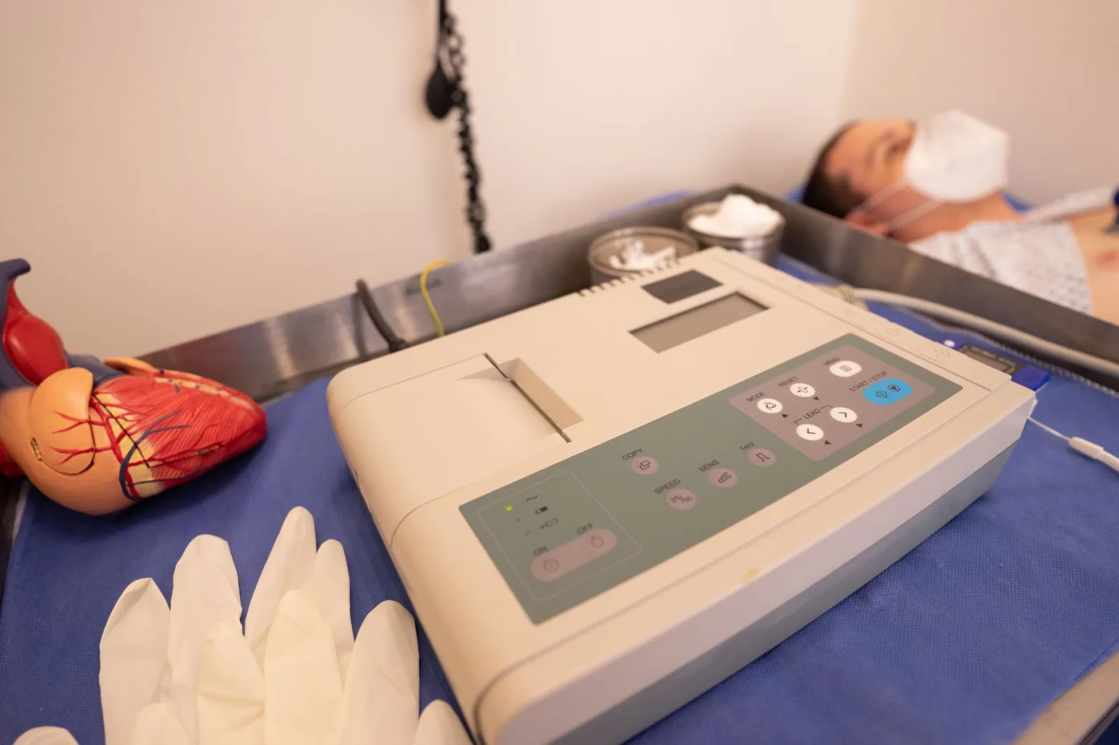 Primer plano de una máquina de ECG y un modelo de corazón en un entorno hospitalario.