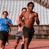 Grupo de atletas entrenando en una pista de atletismo al aire libre, mostrando forma física y determinación.