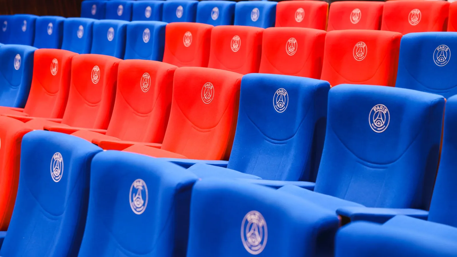 Filas de asientos rojos y azules del estadio con emblemas de París, vibrantes y vacíos.