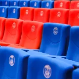 Filas de asientos rojos y azules del estadio con emblemas de París, vibrantes y vacíos.