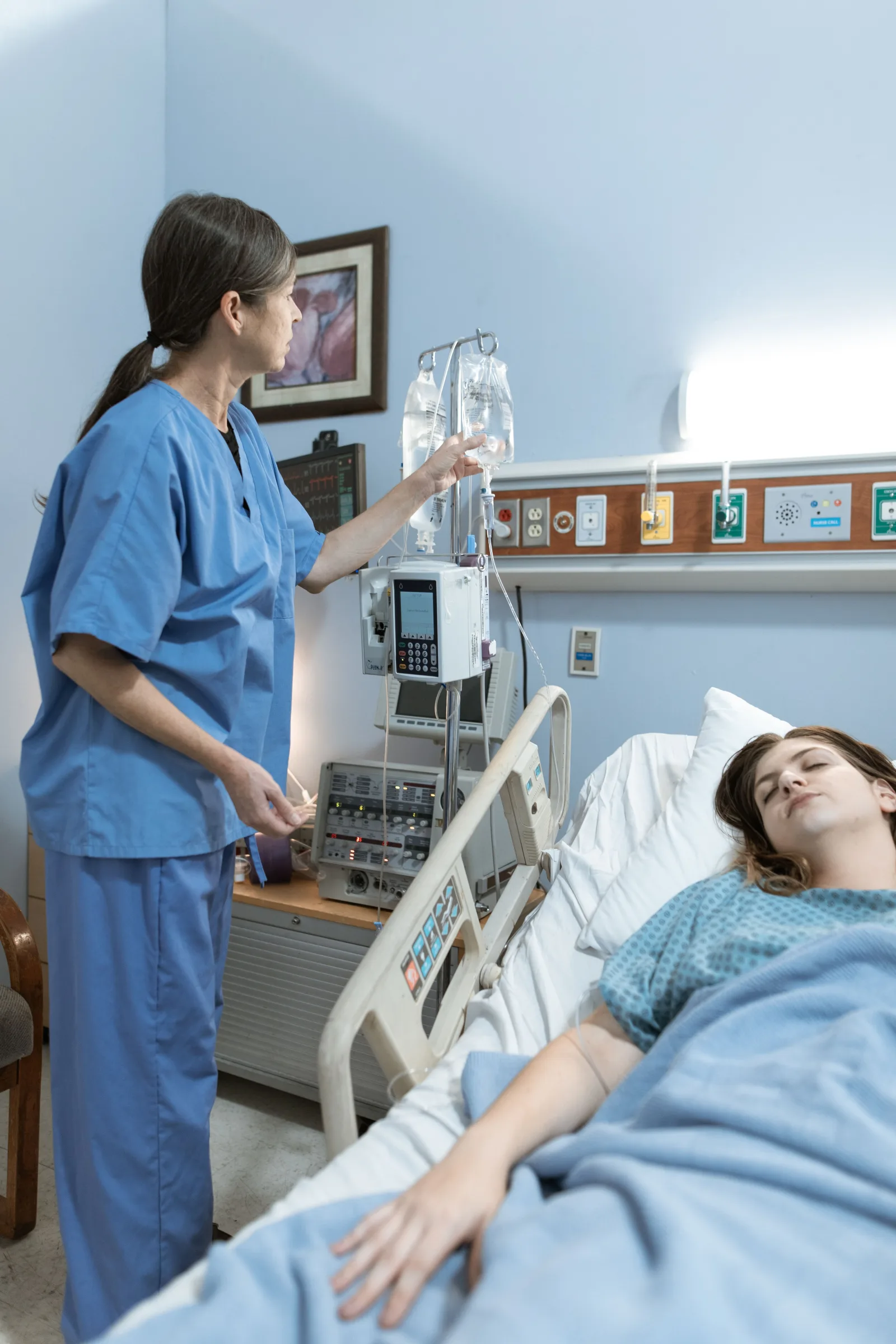 Una enfermera atiende a un paciente en una habitación de hospital, asegurándose de que el equipo médico funcione.