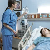 Una enfermera atiende a un paciente en una habitación de hospital, asegurándose de que el equipo médico funcione.