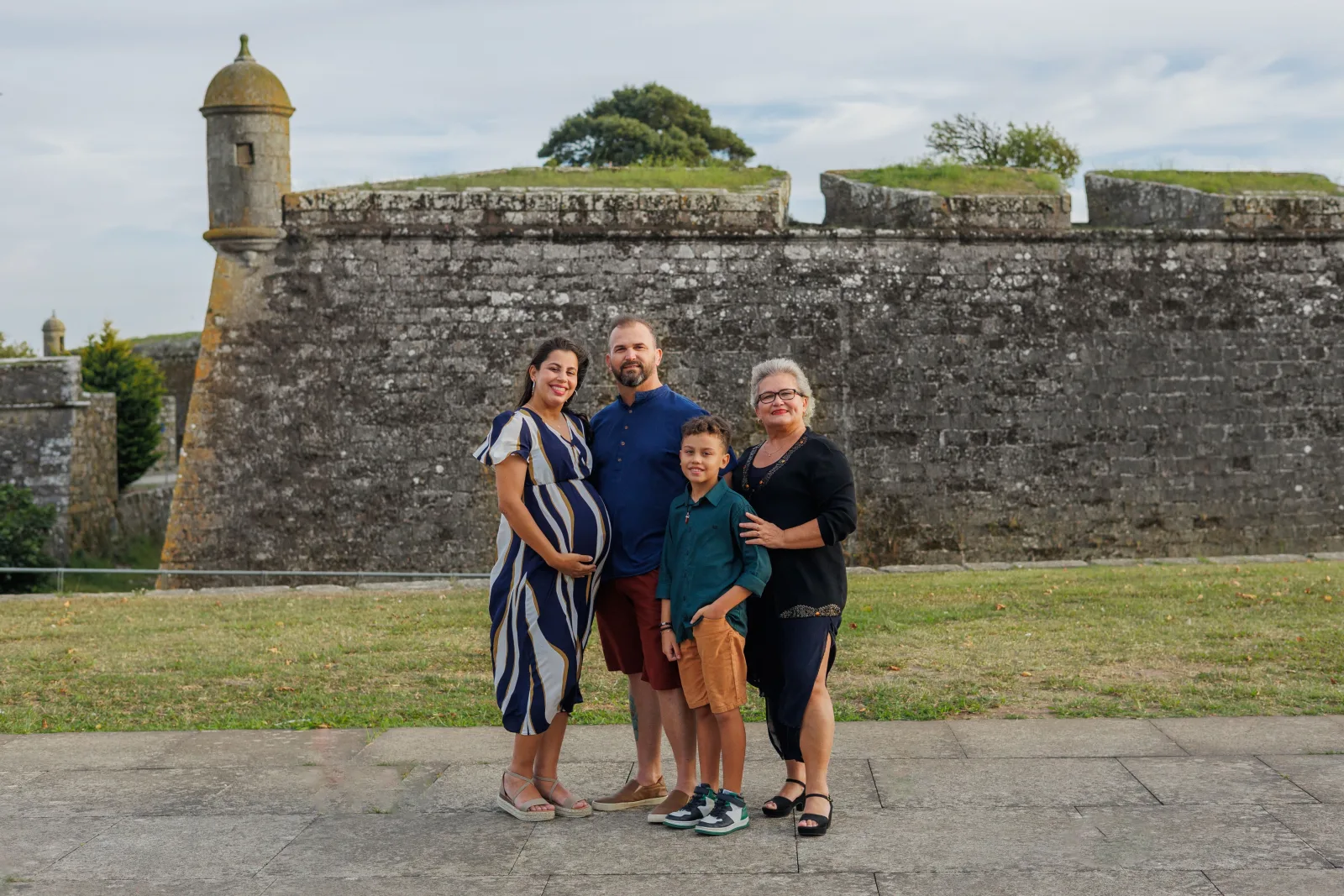 Family posing by a historic fortress wall in Ponte de Lima, Portugal, during a pleasant summer day.