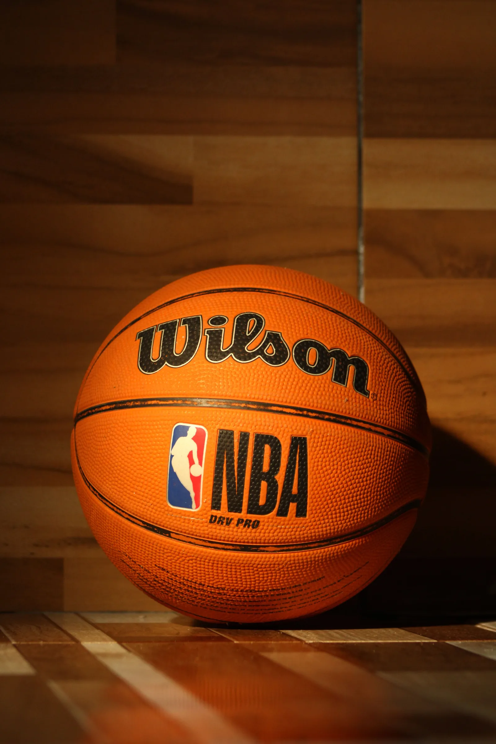 Un balón Wilson de la NBA sobre una cancha de madera pulida con una iluminación dramática.