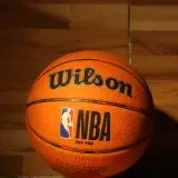 Un balón Wilson de la NBA sobre una cancha de madera pulida con una iluminación dramática.