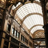 Intrincado interior del histórico Parisi Udvar de Budapest, con un impresionante techo de cristal y detalles ornamentados.