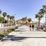 Sunny day on Alicante promenade showcasing the Castillo de Santa Bárbara and palm trees.