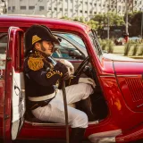 A historic reenactor in uniform sits in a red vintage car on a sunny day in Buenos Aires, Argentina.