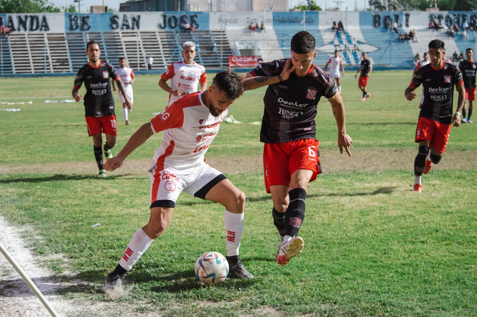 Partido de fútbol competitivo con jugadores en acción en un campo de fútbol al aire libre.