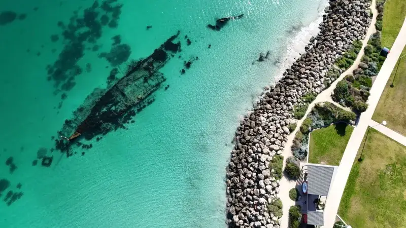 Drone shot of an underwater shipwreck near Perth, Australia with turquoise waters and rocky shoreline.