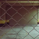 Vista interior borrosa a través de una cerca de malla metálica en un entorno industrial.