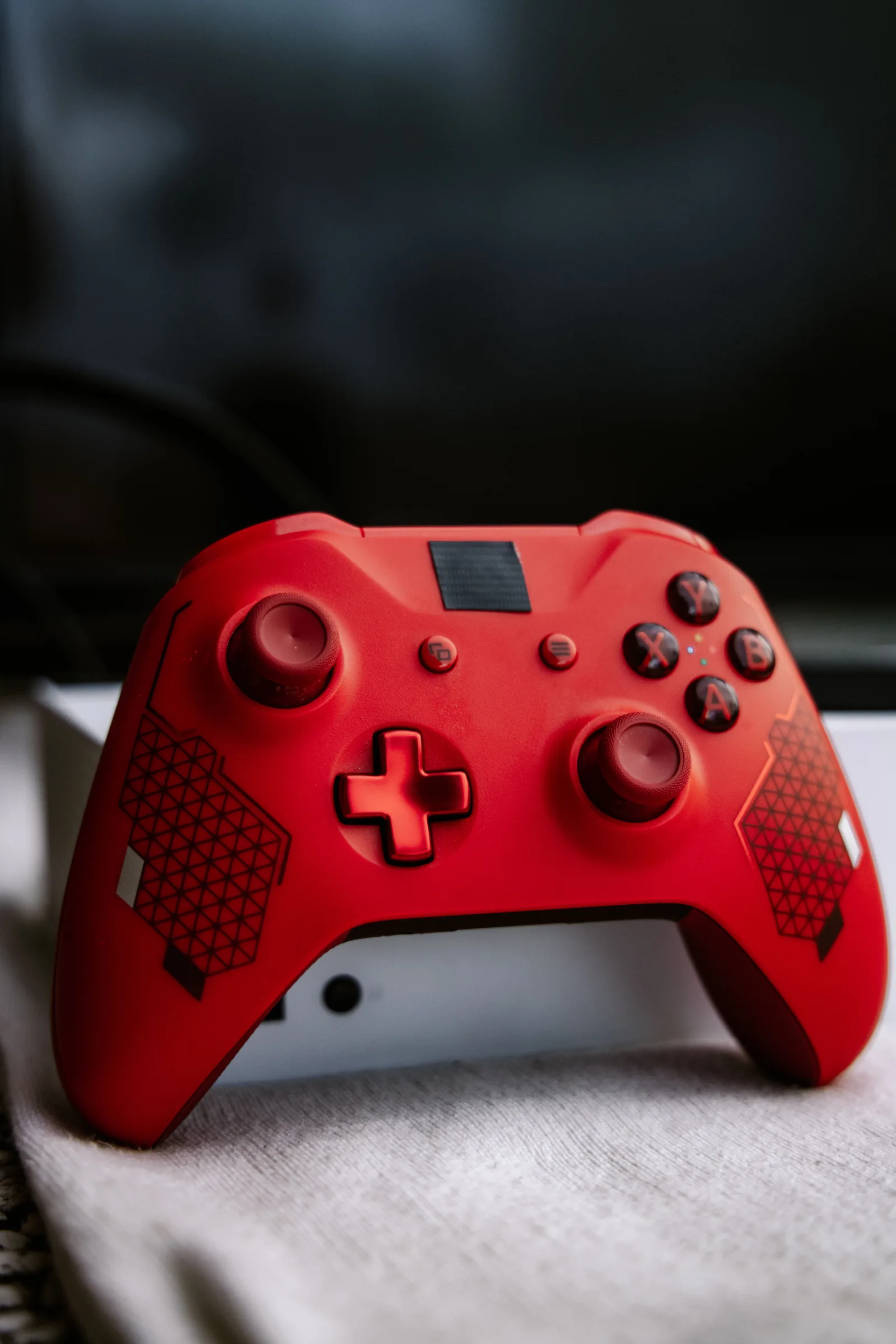 Primer plano de un control de videojuegos Xbox rojo sobre una superficie blanca, ideal para temas de videojuegos.