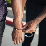 Primer plano de un agente de policía esposando a un sospechoso al aire libre, haciendo cumplir la ley.