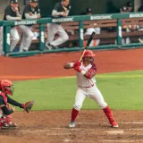 Jugador de béisbol preparado para batear durante un emocionante partido, con el receptor y el árbitro cerca.
