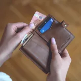 Manos sosteniendo una cartera de cuero con efectivo y una tarjeta de crédito sobre una superficie de madera.
