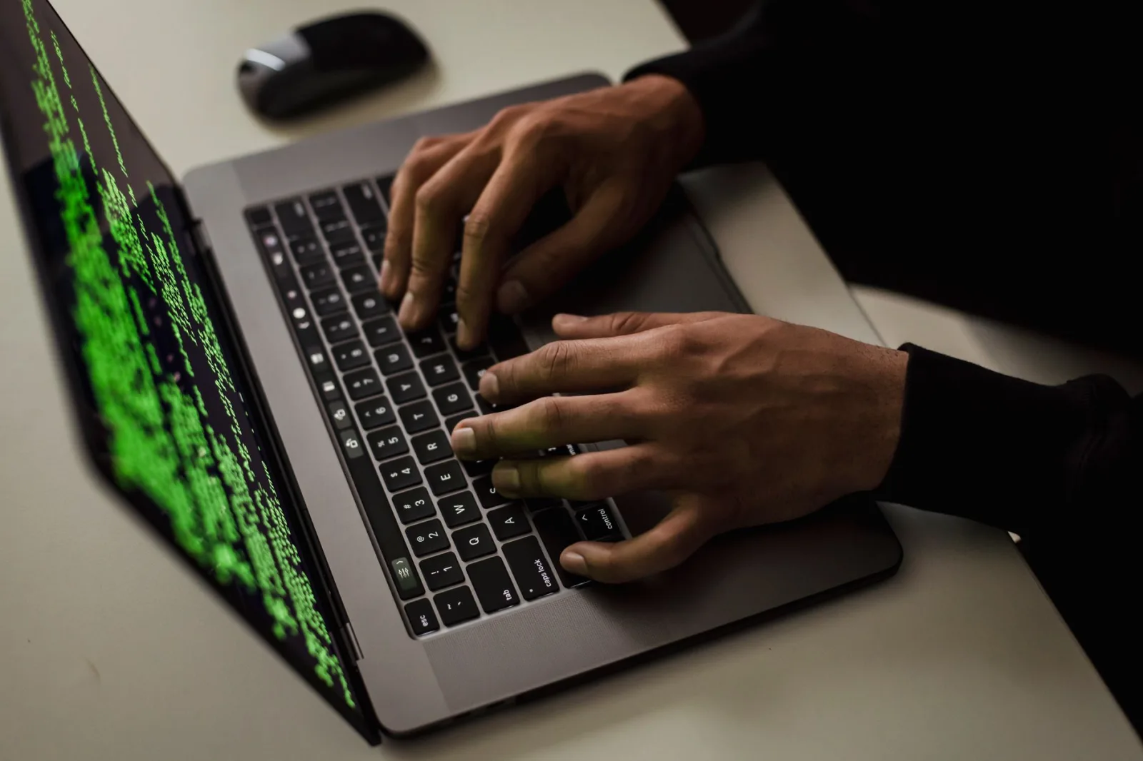 Vista desde arriba de un hacker anónimo escribiendo en una netbook con datos en pantalla mientras está sentado en un escritorio