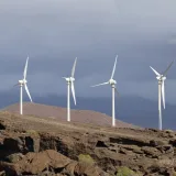 Fila de aerogeneradores en un terreno rocoso bajo un cielo nublado, que muestra la energía renovable.