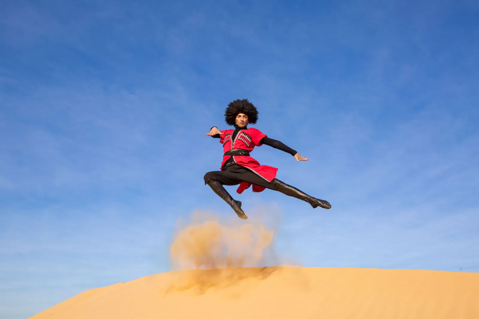 Una bailarina realiza un salto dinámico sobre una duna de arena en el desierto de Dubái.