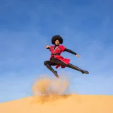 Una bailarina realiza un salto dinámico sobre una duna de arena en el desierto de Dubái.