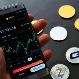 Close-up of a smartphone app showing Bitcoin trading details with crypto coins on a black surface.
