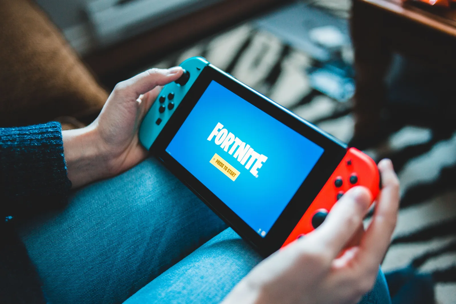 Primer plano de unas manos sosteniendo una Nintendo Switch con la pantalla del juego Fortnite en interiores.