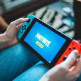 Primer plano de unas manos sosteniendo una Nintendo Switch con la pantalla del juego Fortnite en interiores.