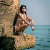 Mujer joven en cuclillas sobre una roca junto al mar en Puerto Cabello, Venezuela.