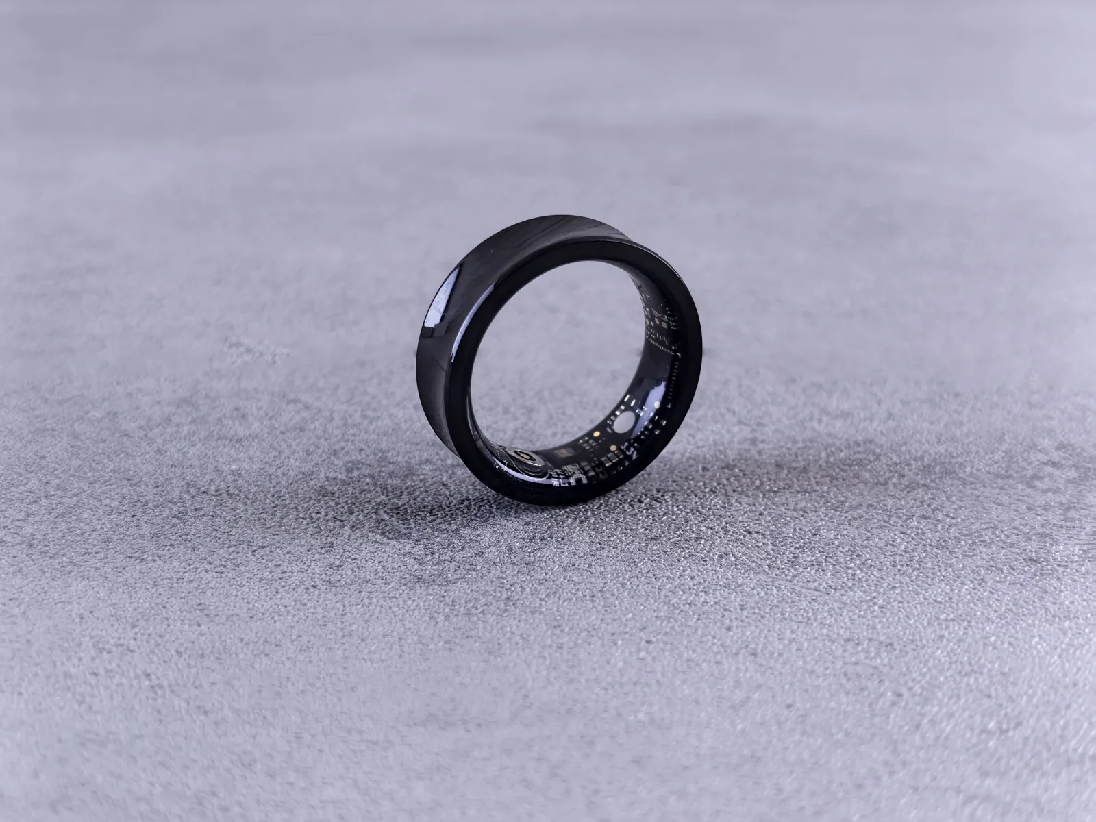 Un anillo inteligente moderno de color negro, con circuitos visibles, sobre una superficie de concreto texturizada.