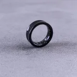 Un anillo inteligente moderno de color negro, con circuitos visibles, sobre una superficie de concreto texturizada.