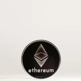 Close-up of an Ethereum cryptocurrency coin with a minimalist design on a reflective surface.