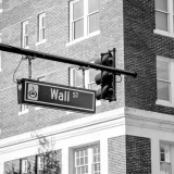 Imagen en escala de grises de la señal de Wall Street con semáforos frente a un edificio de ladrillo.
