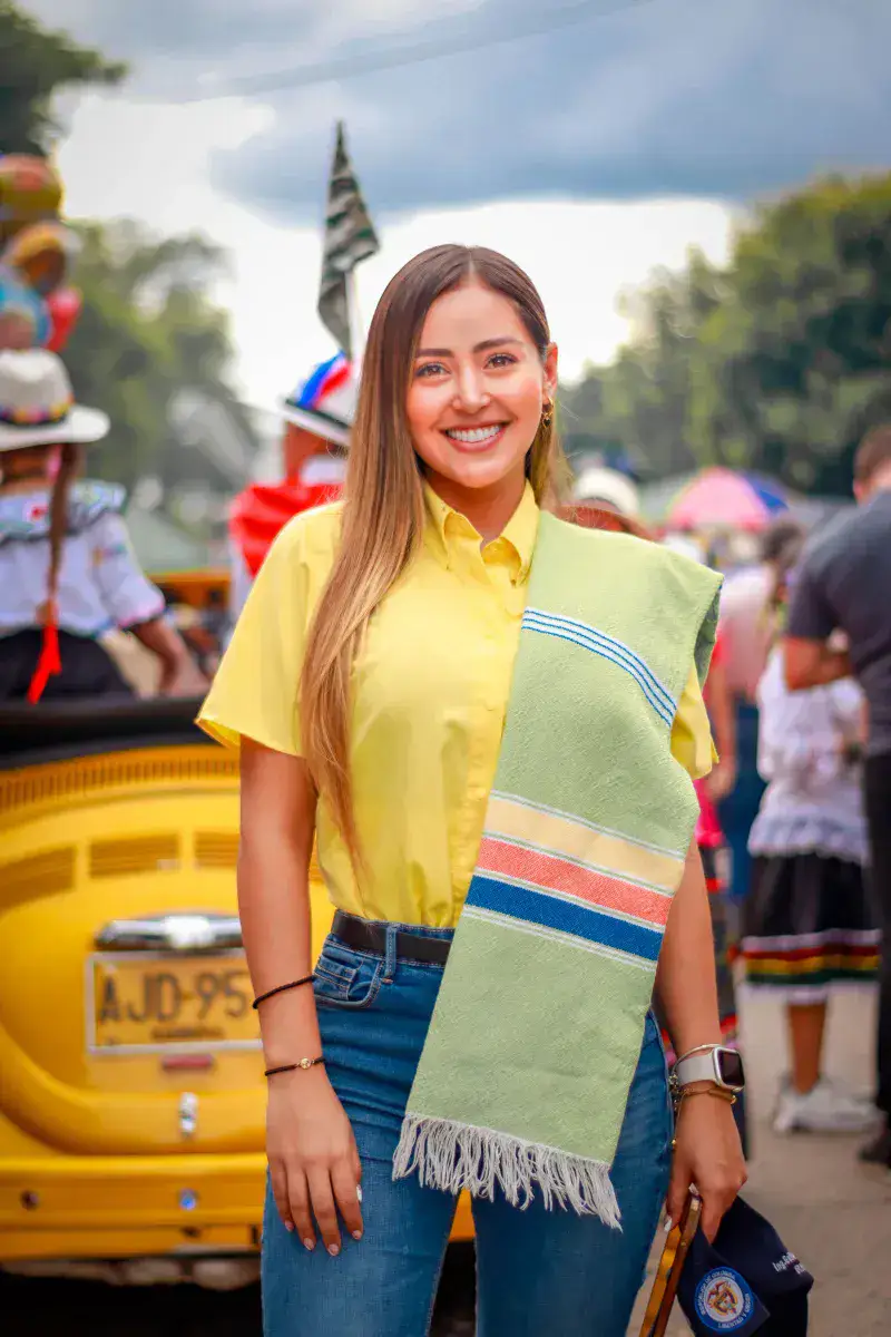 A cheerful woman in a yellow shirt at a colorful festival parade in Villanueva, Colombia.