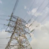 Vista de cerca de una torre y líneas de transmisión de alto voltaje contra un cielo nublado.