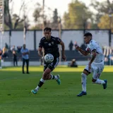 Acción intensa de un partido de fútbol con dos jugadores compitiendo ferozmente bajo el sol.
