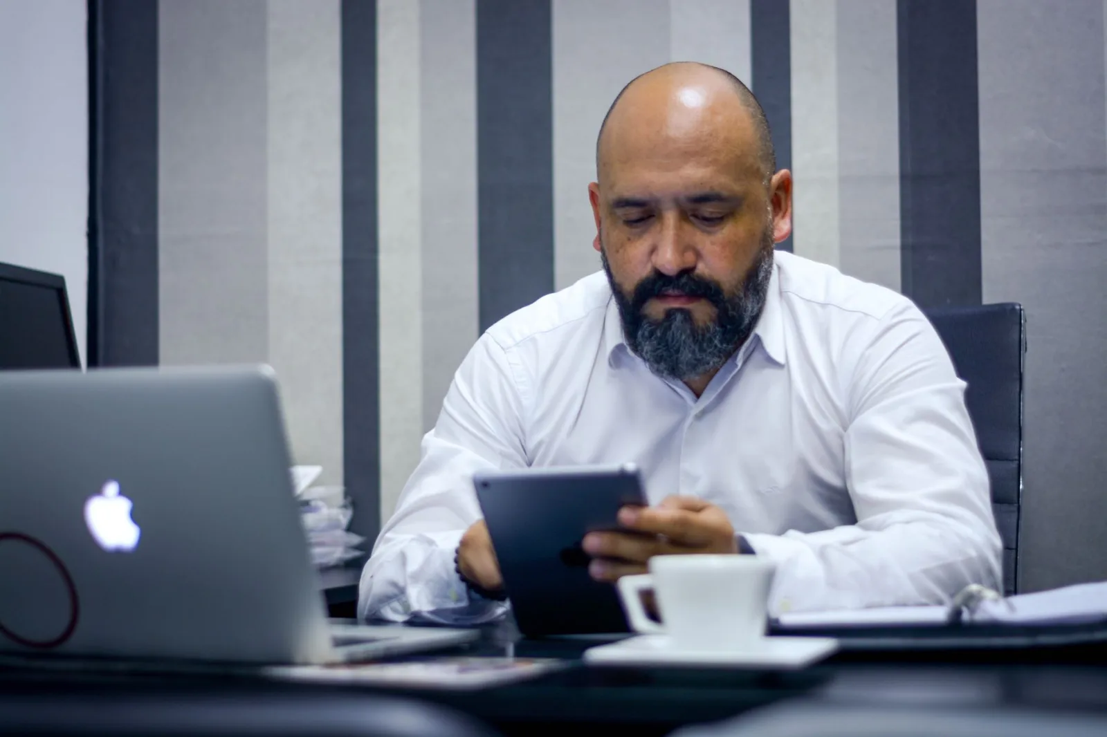 Hombre barbudo usando una tableta en una oficina moderna, centrado en la tecnología y la productividad.