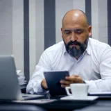 Hombre barbudo usando una tableta en una oficina moderna, centrado en la tecnología y la productividad.