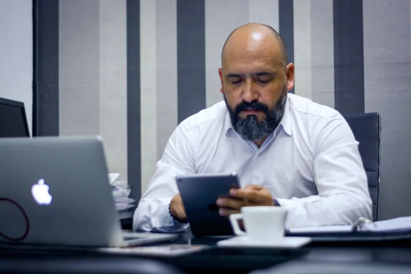 Hombre barbudo usando una tableta en una oficina moderna, centrado en la tecnología y la productividad.