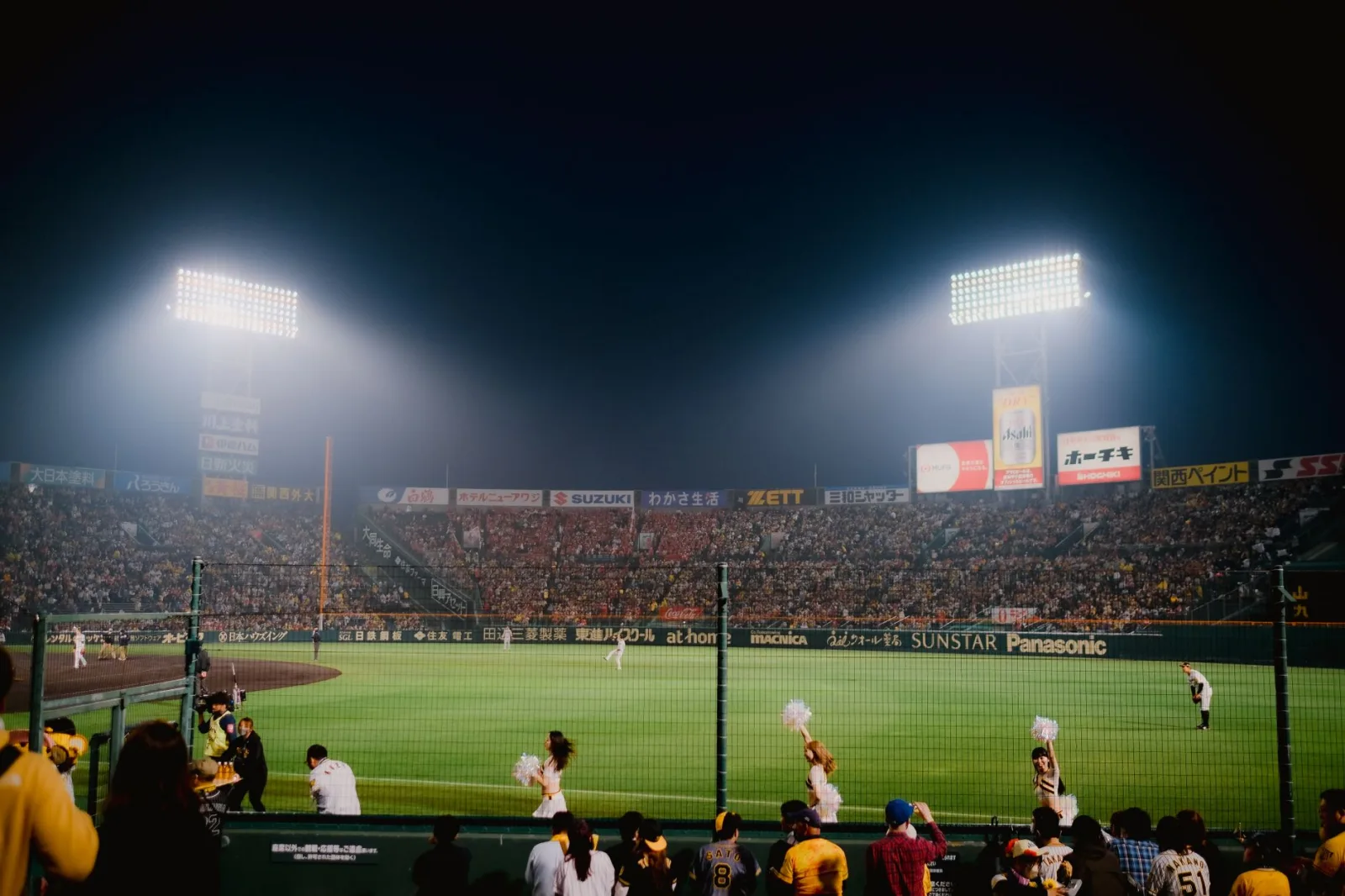 Emocionante partido de béisbol nocturno en el estadio Hanshin Koshien de Japón, con un público lleno de energía.