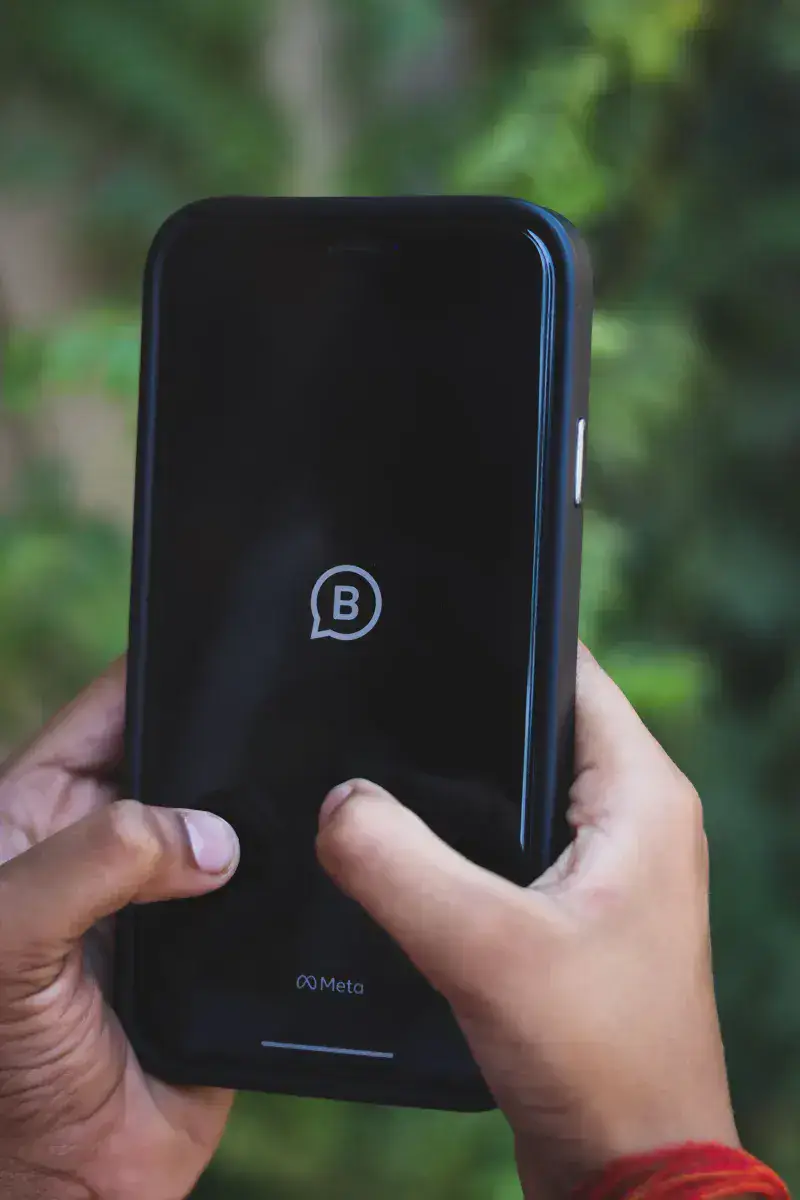 Close-up of hands holding a smartphone with Meta logo outdoors against green background.