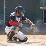 Receptor de béisbol listo para atrapar un lanzamiento durante un partido al aire libre y soleado.