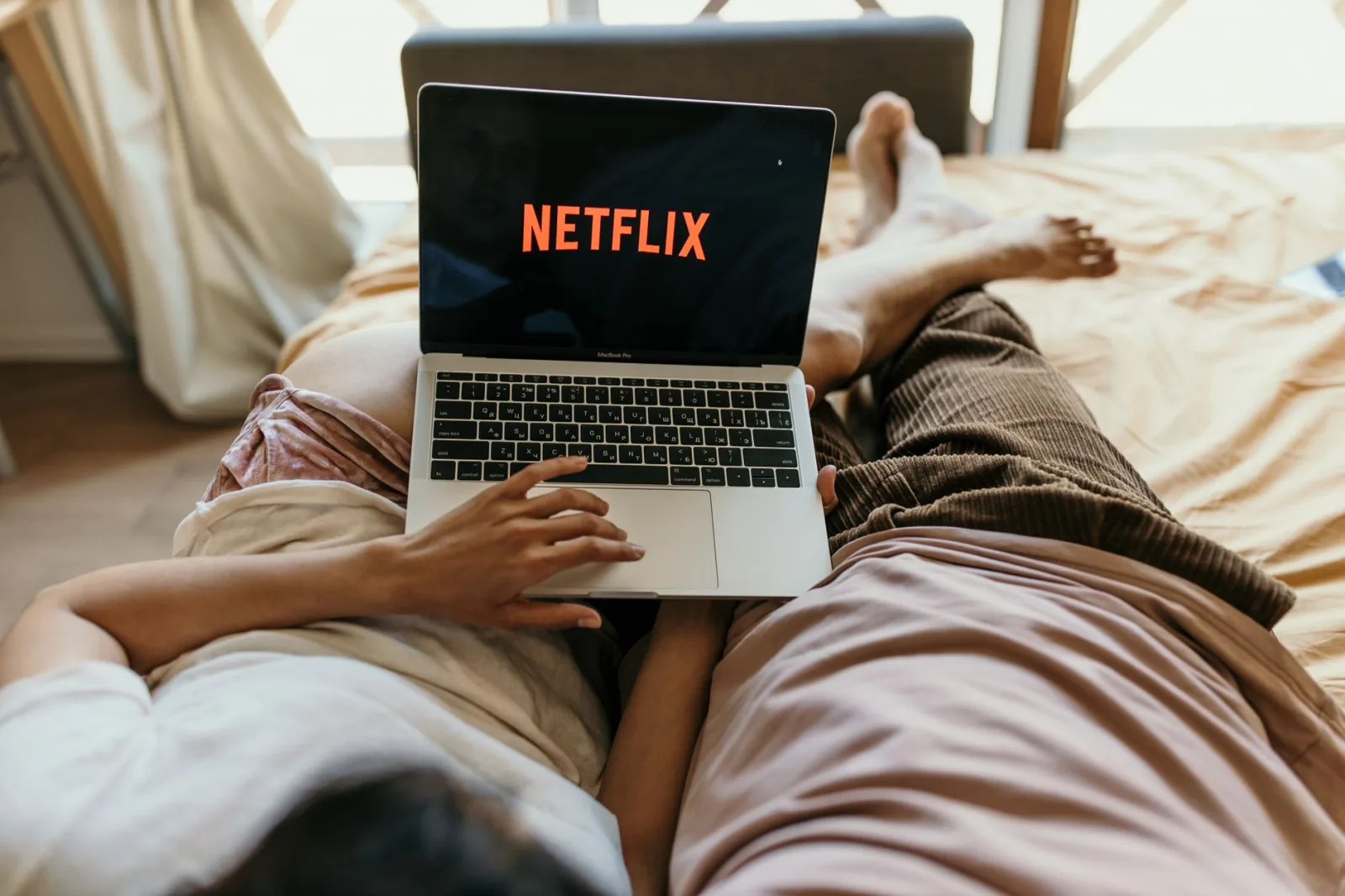 Una pareja recostada cómodamente en la cama viendo Netflix en una laptop, disfrutando de su tiempo libre juntos en casa.