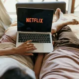 Una pareja recostada cómodamente en la cama viendo Netflix en una laptop, disfrutando de su tiempo libre juntos en casa.
