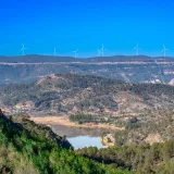 Paisaje pintoresco de un parque eólico en Cofrentes, España, con abundante vegetación y un cielo azul despejado.