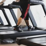 Una persona caminando en una cinta de correr en un gimnasio moderno, concentrada en su entrenamiento físico.