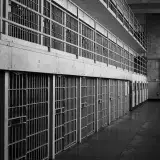 Monochrome image of an empty prison row with steel bars and walkways.