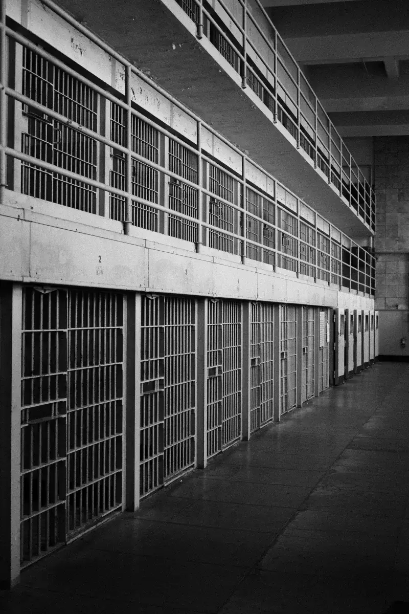 Monochrome image of an empty prison row with steel bars and walkways.