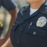 Primer plano de agentes de policía uniformados, mostrando una placa y una radio al aire libre.