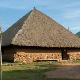 A traditional indigenous hut with a thatched roof in Pueblo Bello, set against a mountain backdrop.