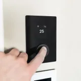 Close-up of a hand adjusting a sleek, modern smart thermostat on a wall.