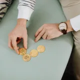 Close-up of hands holding bitcoin coins on a green sofa, emphasizing digital currency trends.